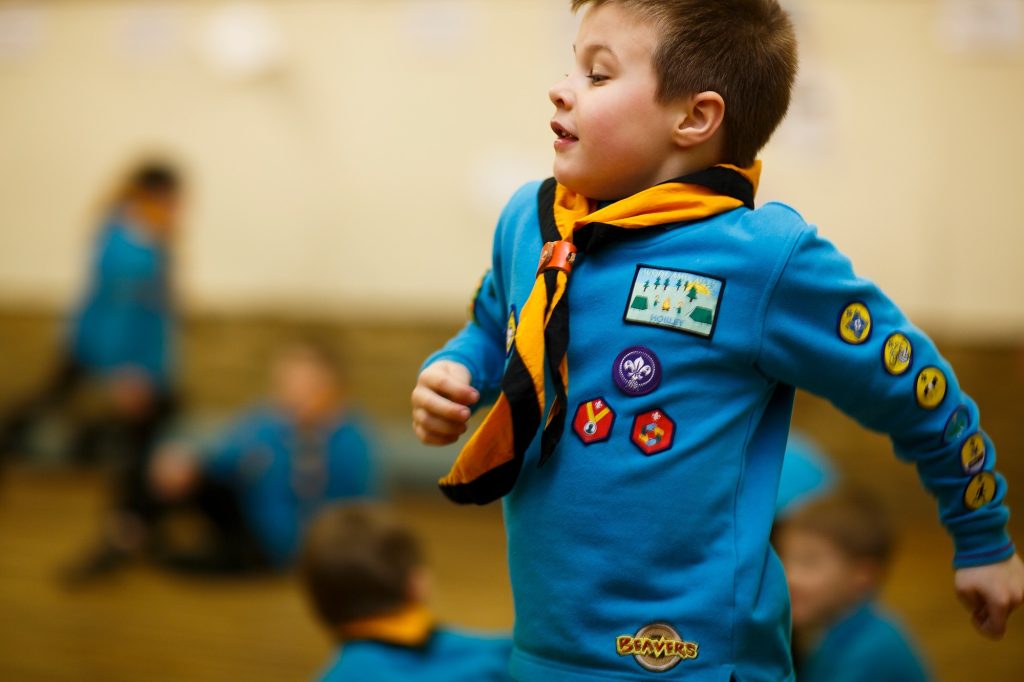A beaver running across a scout hall, wearing his uniform
